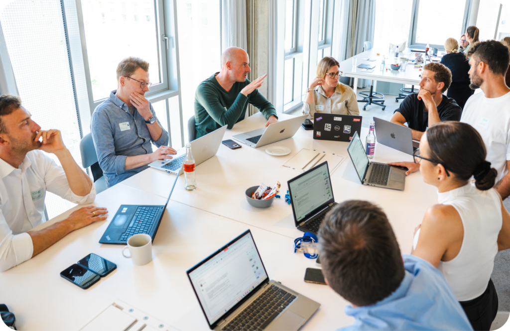 Scotty CEO, Reiner Bruns, in a green sweater, talks with the talentsconnect team around a shared table of laptops during a working session.
