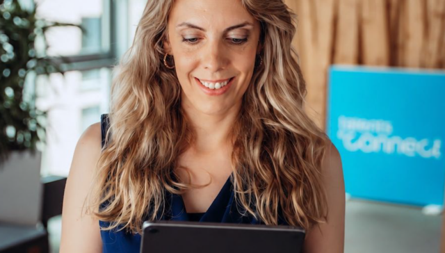 Samira Helbig, Chief Hybrid Resources Officer at talentsconnect, smiles while reading a tablet marked “CHyRO Logbook” in the talentsconnect office.